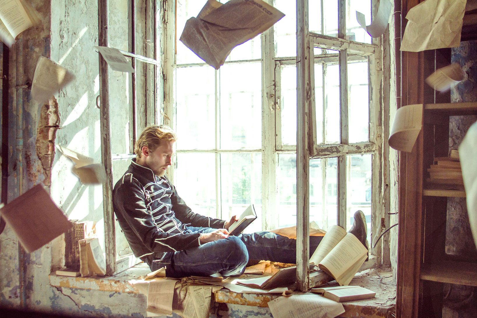 A man is reading a book in a abandoned library while sheets are falling from the ceiling